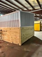 Loafing shed with metal upper and wooden lower siding in indoor setting.