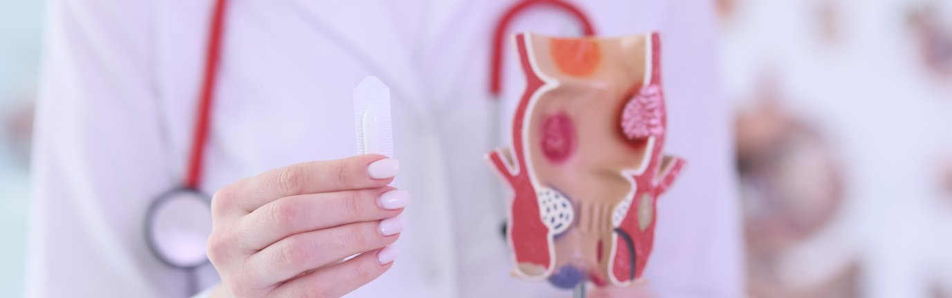 Medico mostra durante una visita proctologica un modellino anatomico e tiene in mano una supposta