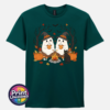 Two ghosts in witch hats holding orange mugs beside a campfire, with a black cat, pumpkins and autumn trees, printed on a unisex T-shirt marine green - Print Unleashed