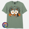 Two ghosts in witch hats holding orange mugs beside a campfire, with a black cat, pumpkins and autumn trees, printed on a unisex T-shirt sage - Print Unleashed
