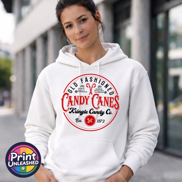 Vintage Kringle Candy Co. candy cane sign with ornate red lettering, crossed candy canes and a five-cent emblem, printed on a white unisex hoodie female model - Print Unleashed