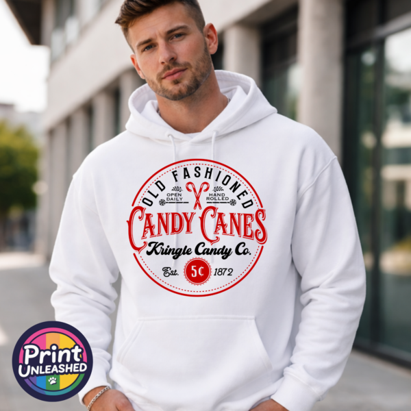 Vintage Kringle Candy Co. candy cane sign with ornate red lettering, crossed candy canes and a five-cent emblem, printed on a white unisex hoodie male model - Print Unleashed