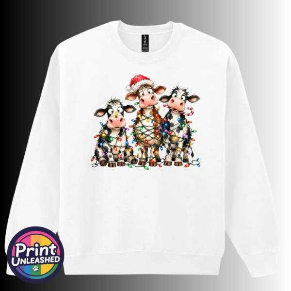 Three wide-eyed Christmas cows tangled in colourful lights, one wearing a Santa hat and another holding a candy cane, printed on a white unisex sweatshirt - Print Unleashed