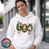 Three Christmas cows in festive wreaths, one wearing a Santa hat and another facing backwards with antlers and striped leg warmers, printed on a white unisex hoodie female model - Print Unleashed