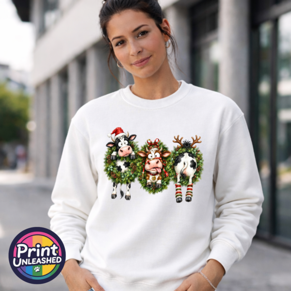 Cow Wreath sweat model female Three Christmas cows in festive wreaths, one wearing a Santa hat and another facing backwards with antlers and striped leg warmers, printed on a white unisex sweatshirt female model - Print Unleashed