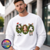 Three Christmas cows in festive wreaths, one wearing a Santa hat and another facing backwards with antlers and striped leg warmers, printed on a white unisex sweatshirt male model - Print Unleashed