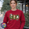 Three Christmas cows in festive wreaths, one wearing a Santa hat and another facing backwards with antlers and striped leg warmers, printed on a cherry red unisex sweatshirt female model - Print Unleashed