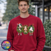 Three Christmas cows in festive wreaths, one wearing a Santa hat and another facing backwards with antlers and striped leg warmers, printed on a cherry red unisex sweatshirt male model - Print Unleashed