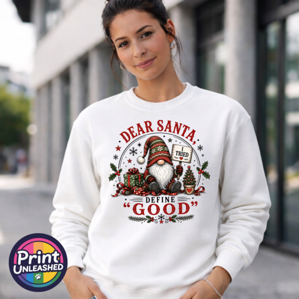 Christmas gonk holding an I Tried sign beside presents and a small tree, with Dear Santa Define Good wording, printed on a white unisex sweatshirt female model - Print Unleashed