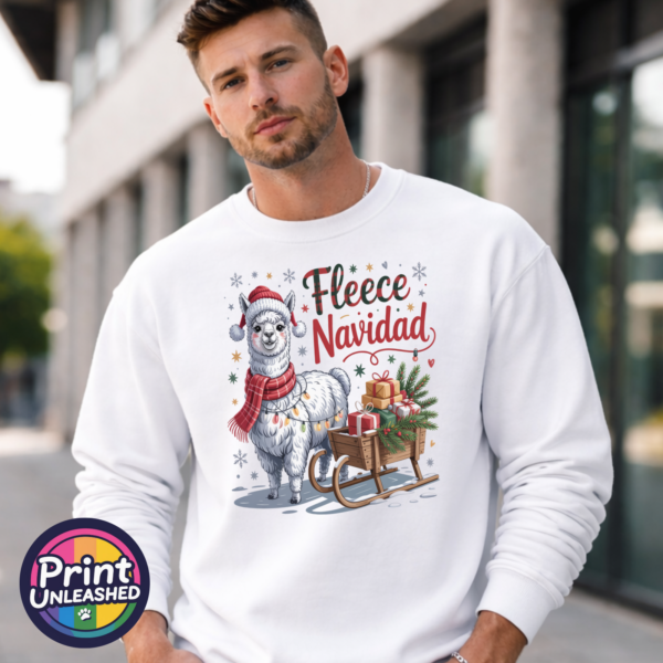 Christmas llama wearing a red knitted hat, tartan scarf and fairy lights beside a gift-filled sleigh, with Fleece Navidad wording on a white unisex sweatshirt male model - Print Unleashed