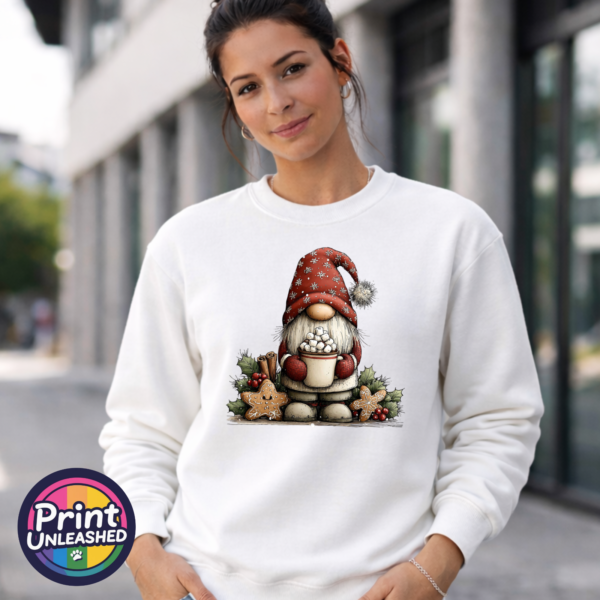 Christmas gonk in a red snowflake-patterned hat holding hot chocolate piled with marshmallows, surrounded by gingerbread stars and holly, printed on a white unisex sweatshirt female model - Print Unleashed