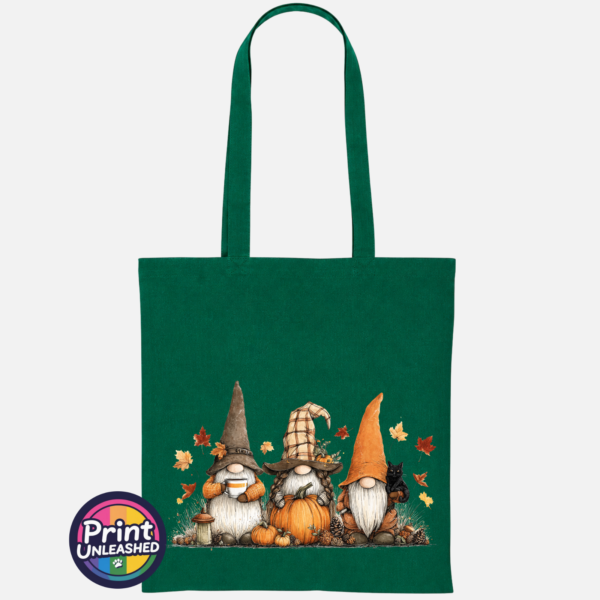 Three autumn gonks in tall pointed hats with pumpkins, a takeaway cup, a black cat and falling leaves printed on a bottle green tote bag - Print Unleashed