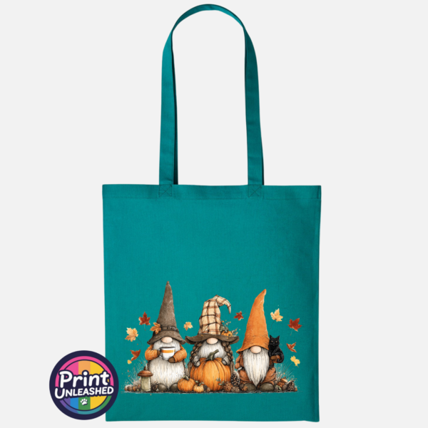 Three autumn gonks in tall pointed hats with pumpkins, a takeaway cup, a black cat and falling leaves printed on a jade tote bag - Print Unleashed