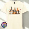 Three autumn gonks in witch hats with pumpkins, a takeaway cup, a black cat and falling leaves printed on a unisex T-shirt off white - Print Unleashed