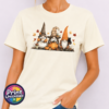 Three autumn gonks in witch hats with pumpkins, a takeaway cup, a black cat and falling leaves printed on a unisex T-shirt off white model - Print Unleashed