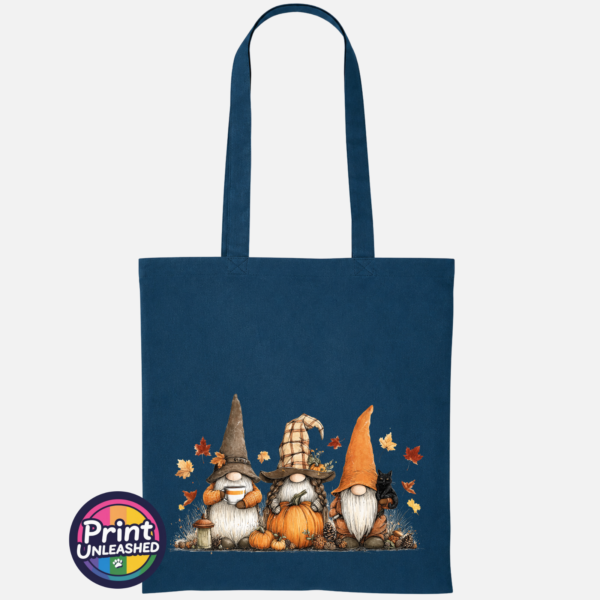 Three autumn gonks in tall pointed hats with pumpkins, a takeaway cup, a black cat and falling leaves printed on a petrol tote bag - Print Unleashed