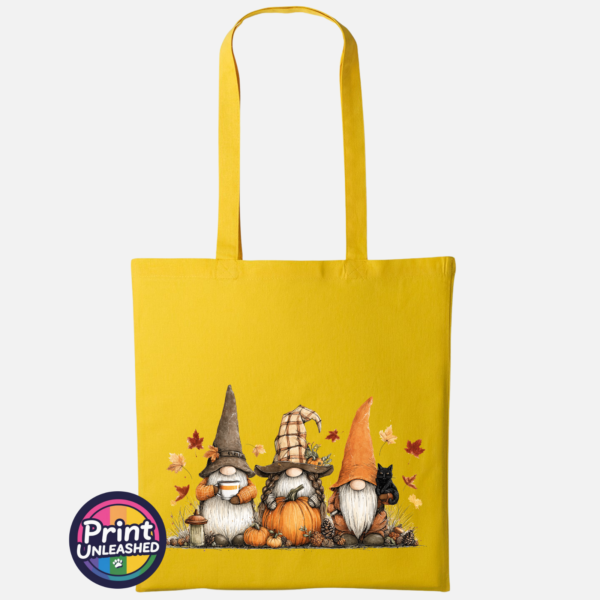 Three autumn gonks in tall pointed hats with pumpkins, a takeaway cup, a black cat and falling leaves printed on a sunflower yellow tote bag - Print Unleashed