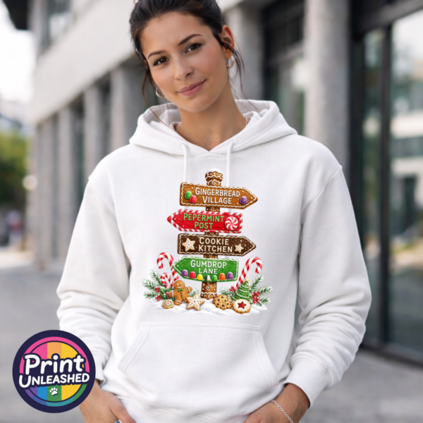 Gingerbread-style signpost pointing to Gingerbread Village, Peppermint Post, Cookie Kitchen and Gumdrop Lane, with sweets and biscuits, printed on a white unisex hoodie female model - Print Unleashed