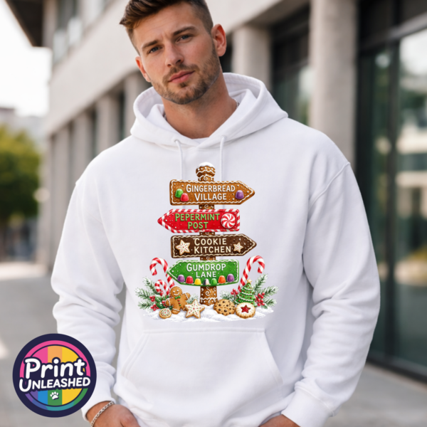 Gingerbread-style signpost pointing to Gingerbread Village, Peppermint Post, Cookie Kitchen and Gumdrop Lane, with sweets and biscuits, printed on a white unisex hoodie male model - Print Unleashed