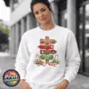 Gingerbread-style signpost pointing to Gingerbread Village, Peppermint Post, Cookie Kitchen and Gumdrop Lane, with sweets and biscuits, printed on a white unisex sweatshirt female model - Print Unleashed