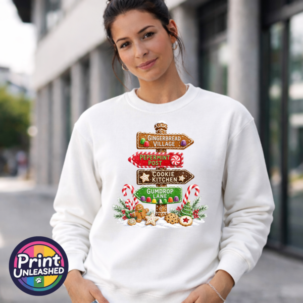 Gumdrop Lane sweat female model Gingerbread-style signpost pointing to Gingerbread Village, Peppermint Post, Cookie Kitchen and Gumdrop Lane, with sweets and biscuits, printed on a white unisex sweatshirt female model - Print Unleashed