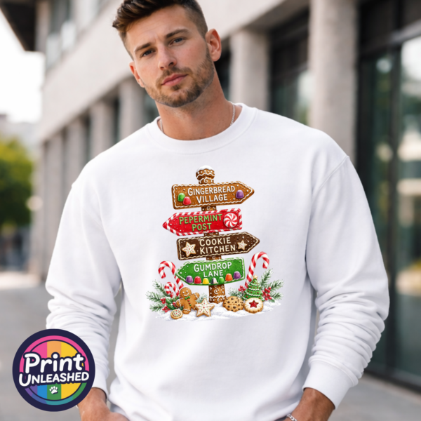 Gumdrop Lane sweat male model Gingerbread-style signpost pointing to Gingerbread Village, Peppermint Post, Cookie Kitchen and Gumdrop Lane, with sweets and biscuits, printed on a white unisex sweatshirt male model - Print Unleashed