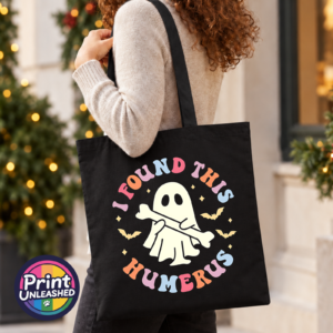 Cute ghost holding a bone beneath colourful I Found This Humerus lettering, surrounded by bats and stars, printed on a tote bag model - Print Unleashed