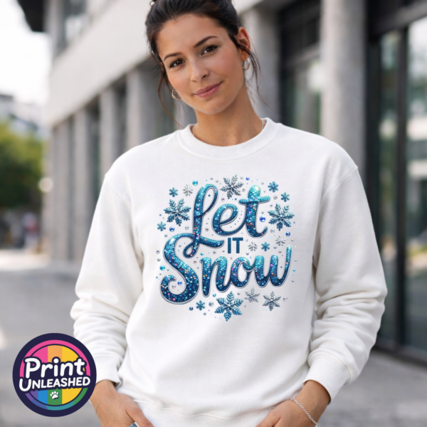 Let It Snow female model Let It Snow wording in blue sequin-effect lettering surrounded by blue and silver snowflakes and jewel-like details printed on a white unisex sweatshirt model image - Print Unleashed