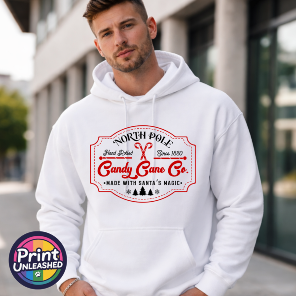 Vintage North Pole Candy Cane Co. design with crossed candy canes, decorative red borders, fir trees and snowflakes, printed on a white unisex hoodie male model - Print Unleashed