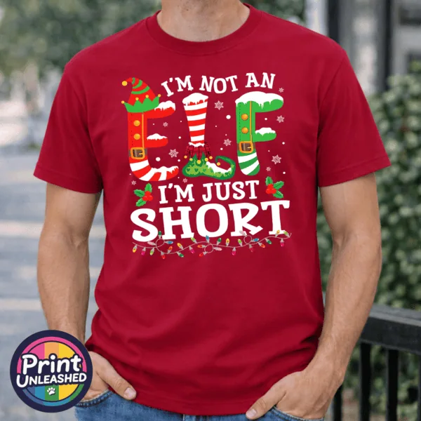 I’m not an elf I’m just short wording with red and green elf-style letters, striped stockings, holly and Christmas lights printed on a cherry red premium unisex T-shirt male model - Print Unleashed