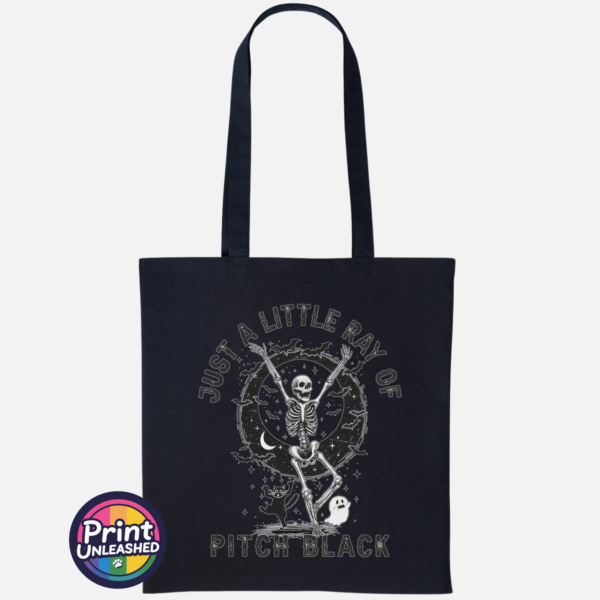 Pitch Black black Black tote bag featuring a dancing skeleton surrounded by bats, stars, a crescent moon, a cat and ghost with Just a Little Ray of Pitch Black lettering - Print Unleashed