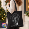 Model image of a black tote bag featuring a dancing skeleton surrounded by bats, stars, a crescent moon, a cat and ghost with Just a Little Ray of Pitch Black lettering - Print Unleashed