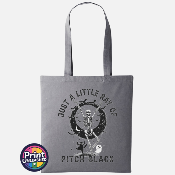 Pitch Black slate Slate tote bag featuring a dancing skeleton surrounded by bats, stars, a crescent moon, a cat and ghost with Just a Little Ray of Pitch Black lettering - Print Unleashed