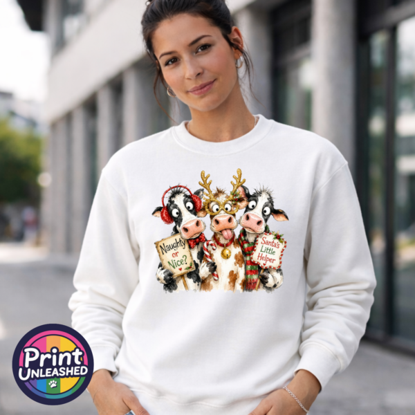 Three Christmas cows with reindeer antlers, earmuffs and signs reading Naughty or Nice and Santa’s Little Helper printed on a white unisex sweatshirt female model - Print Unleashed