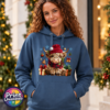 Model wearing a Classic Hoodie featuring a fluffy Highland calf in a red Christmas hat and checked scarf, surrounded by presents and festive decorations, female model - Print Unleashed
