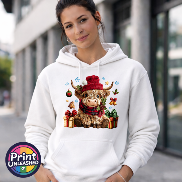 Yarn-style Highland cow wearing a red hat and checked scarf, surrounded by presents, holly, bells and snowflakes, printed on a white unisex hoodie female model - Print Unleashed