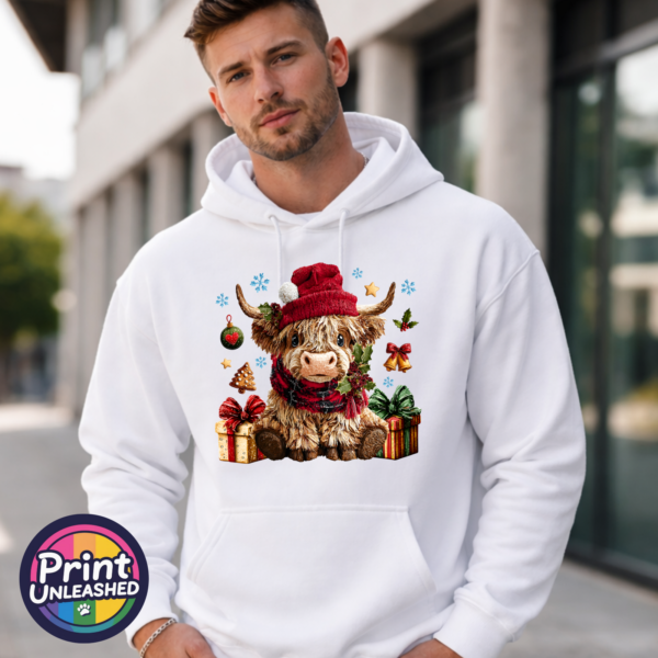 Yarn-style Highland cow wearing a red hat and checked scarf, surrounded by presents, holly, bells and snowflakes, printed on a white unisex hoodie male model - Print Unleashed