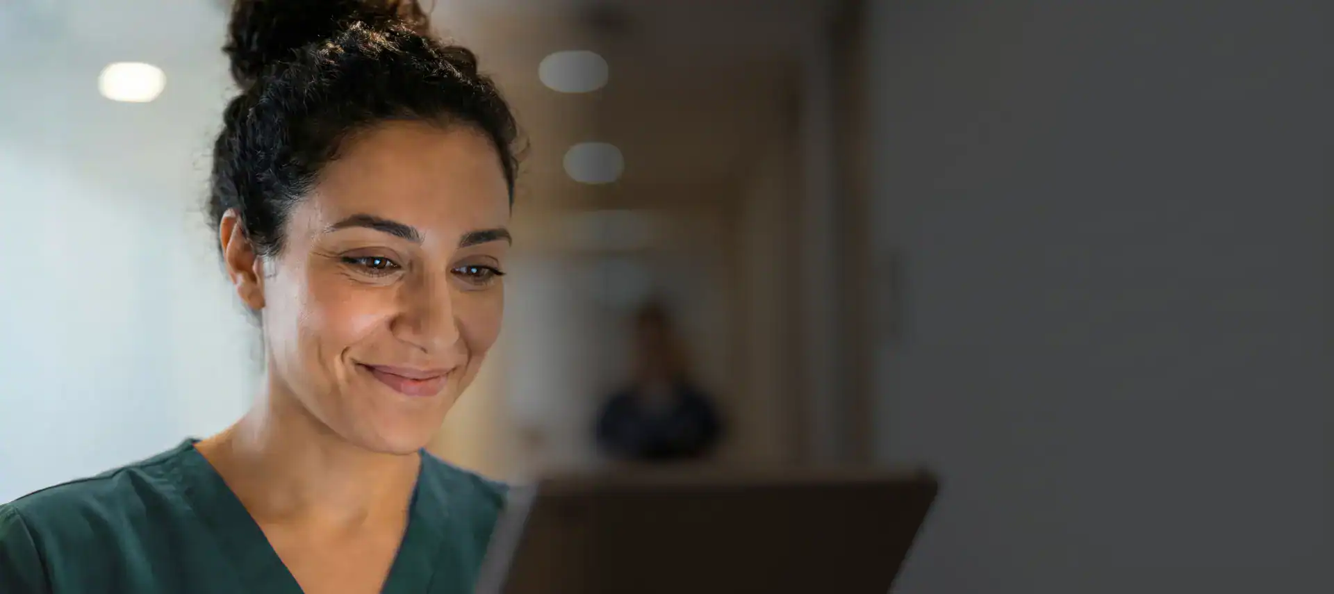 Smiling healthcare worker using a tablet in a medical facility.