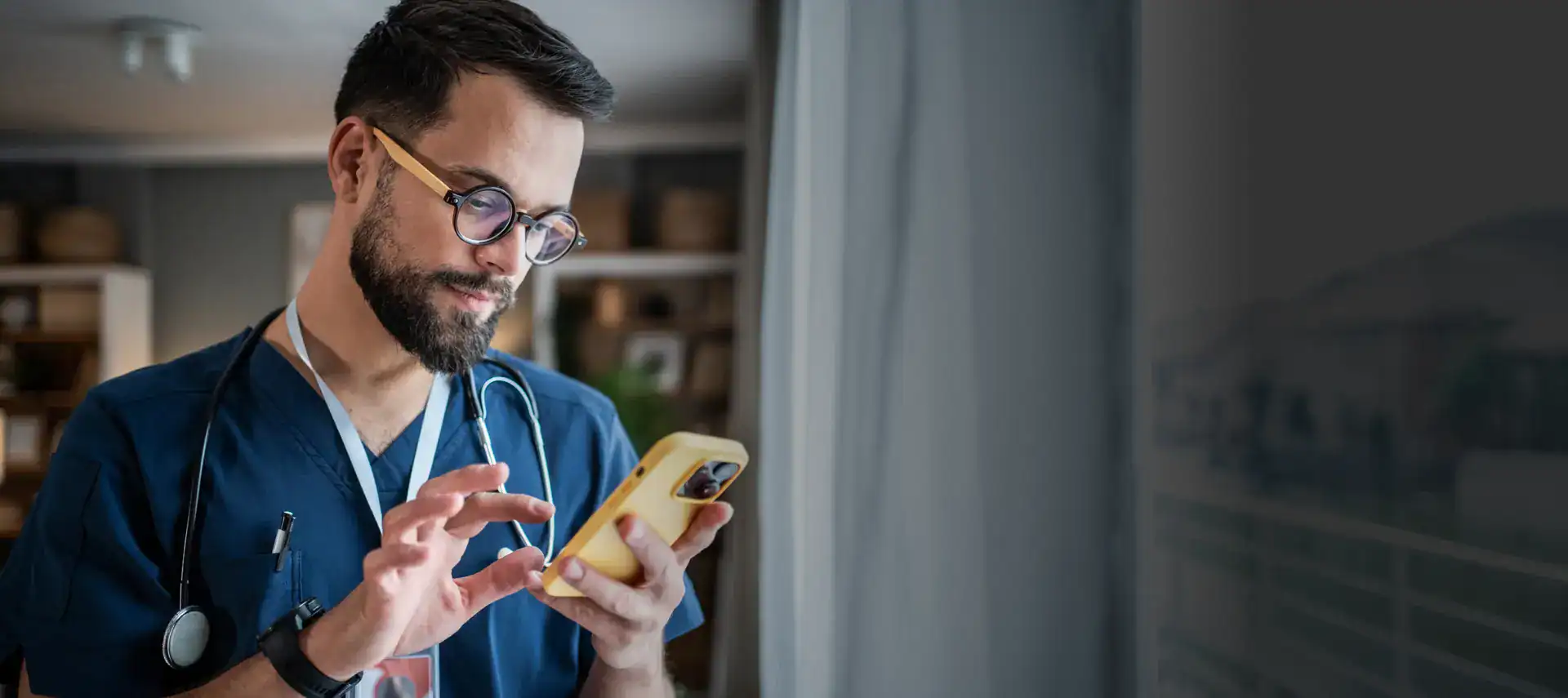 Doctor in scrubs with stethoscope checking phone in clinic.