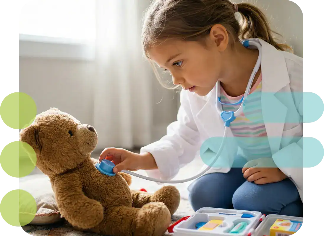 Young girl dressed as a doctor examining teddy bear with toy medical kit.