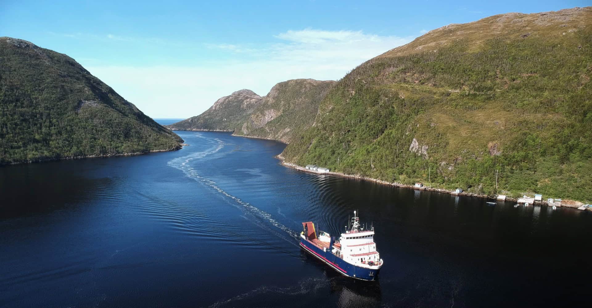 Scenic view of a boat navigating through Newfoundland's fjords surrounded by lush green hills.