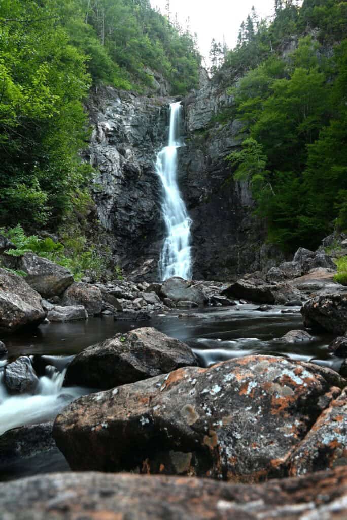 Scenic waterfall in lush green forest with rocks and flowing water.