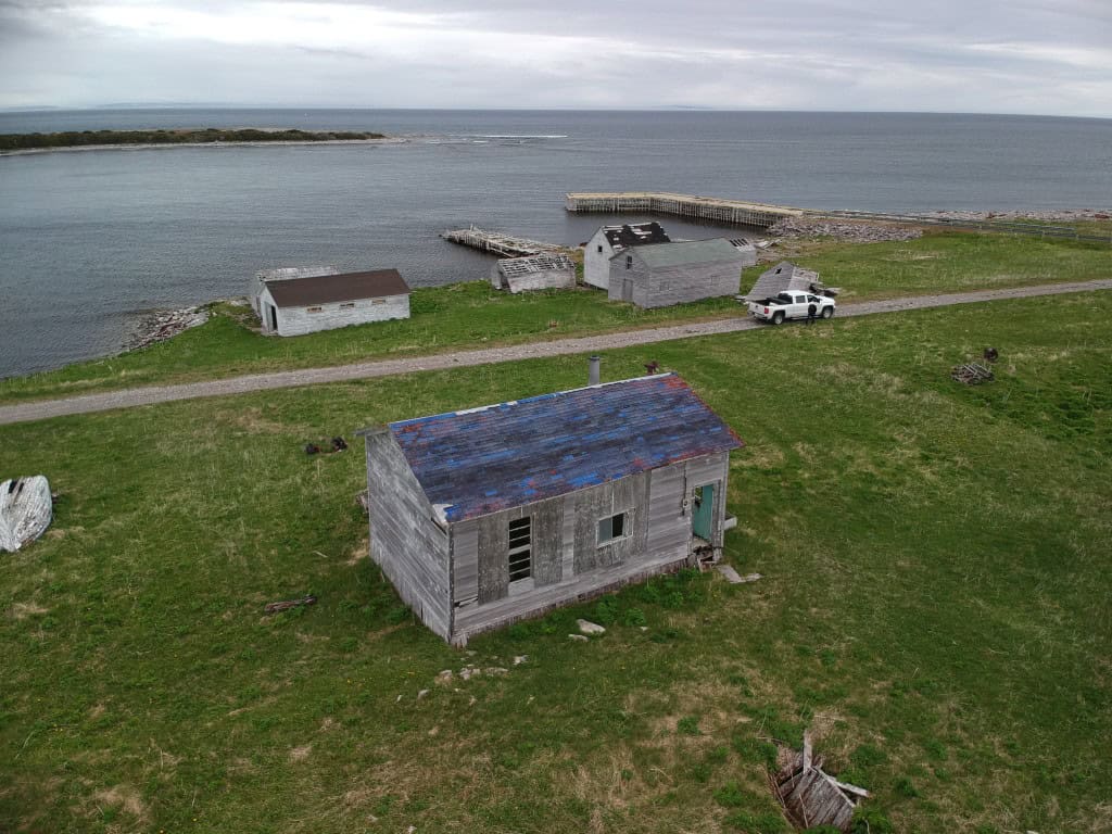 Abandoned buildings along Newfoundland coast with ocean view.