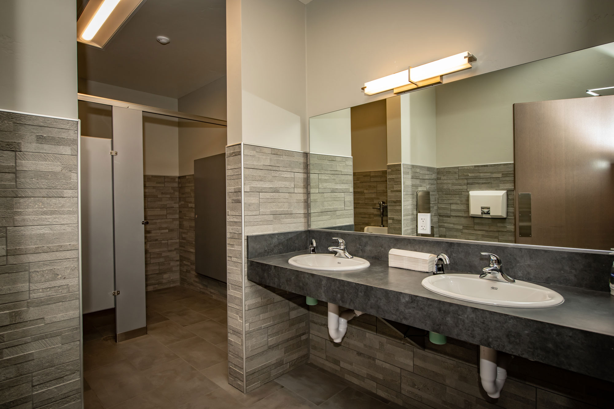 Public restroom with dual sinks, mirror, and tiled wall accents.