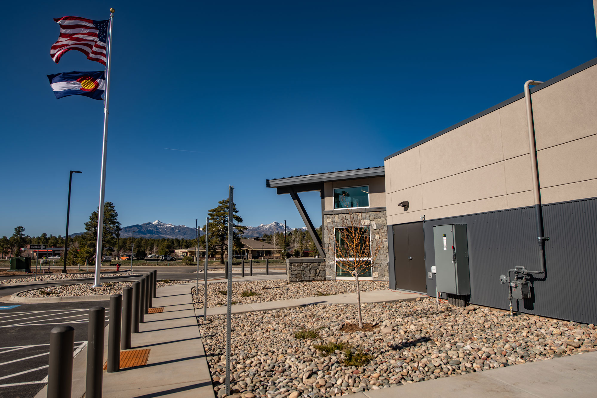 Reynolds Ash + Associates building exterior with flags, clear sky, and mountain backdrop.