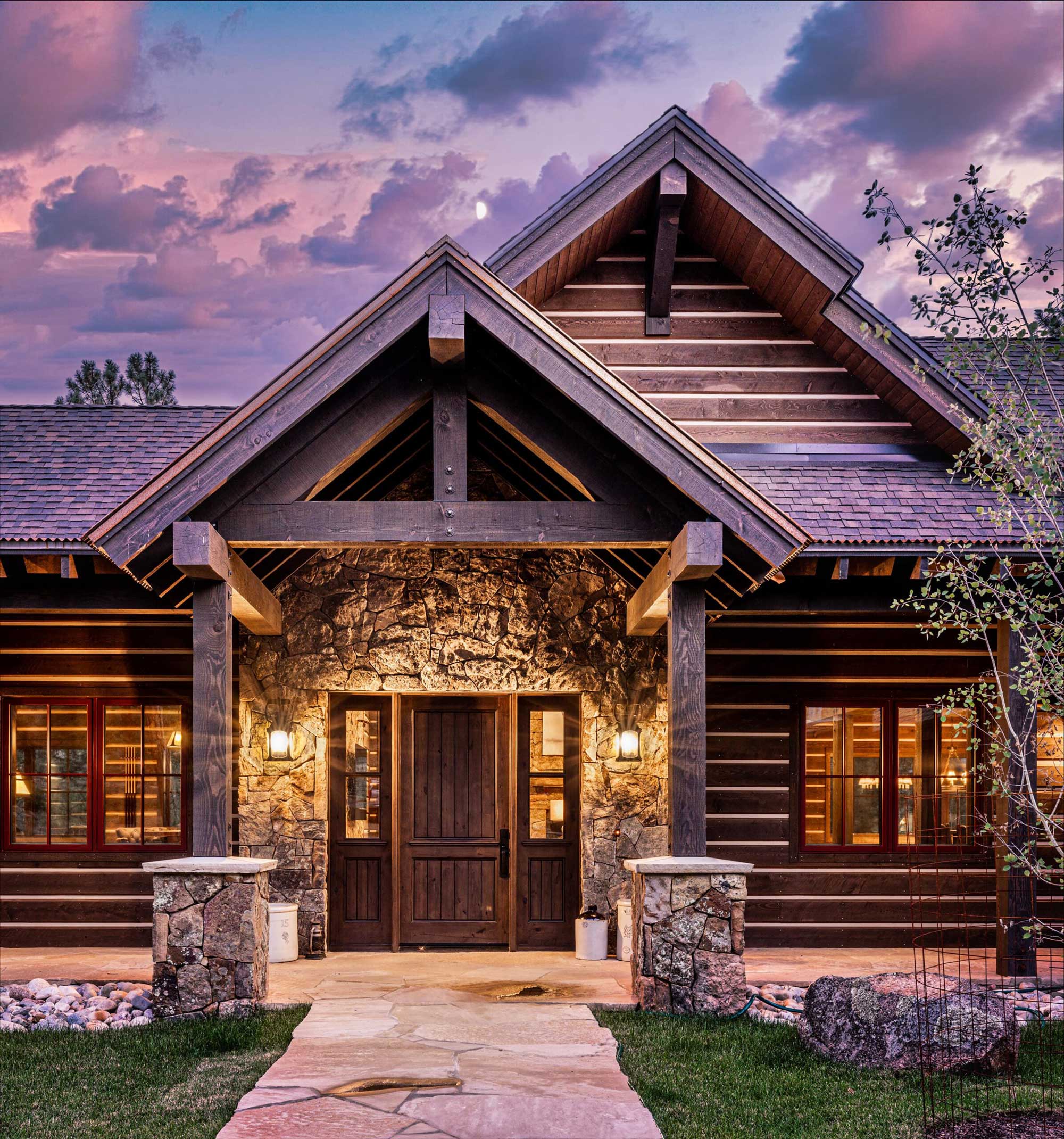 Beautiful log cabin with stone entrance and warm lighting at dusk.