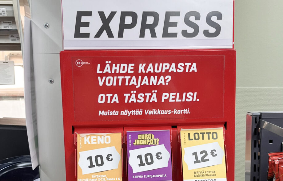 Kuvassa näkyy Veikkauksen kyseenalaiselta näyttävä lottomyyntipiste Salon Turuntien K-Marketissa. Mainos kysyy "Lähde kaupasta voittajana?" ja sitten toteaa "Ota tästä pelisi", minkä alla näkyy lotto- ja Eurojackpot-kuponkeja.
