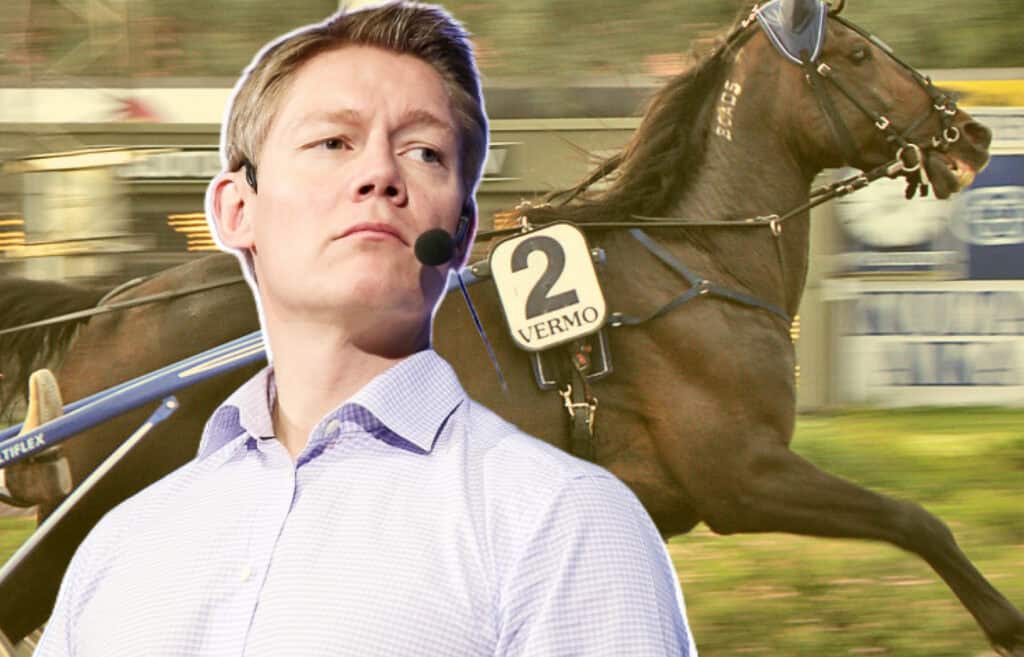 Hans Lord Skarplöth puhuu mikrofonilla, taustalla ravirata ja kilpaileva hevonen numerolla 2 Vermon raviradalla.