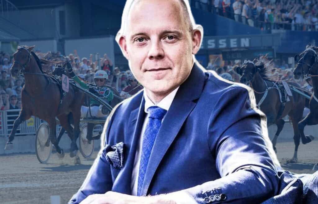Jarkko Nordlund katsoo kameraan puku yllään, taustalla suomalainen ravikilpailu ja ohjastaja radalla.