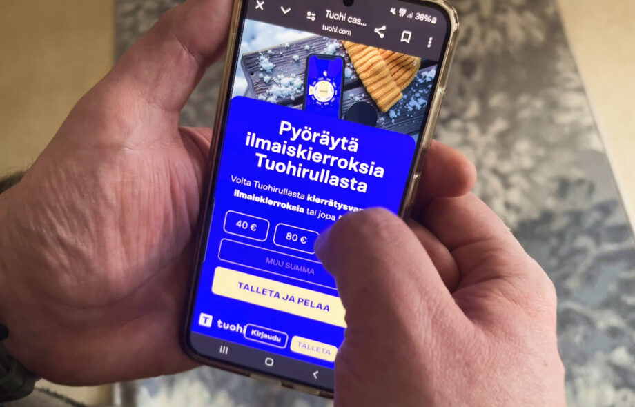 Kuvassa pelaajan kädessä puhelin missä on auki Tuohi Kasinon etusivu ja rekisteröitymisvapaa talletusmoduuli.